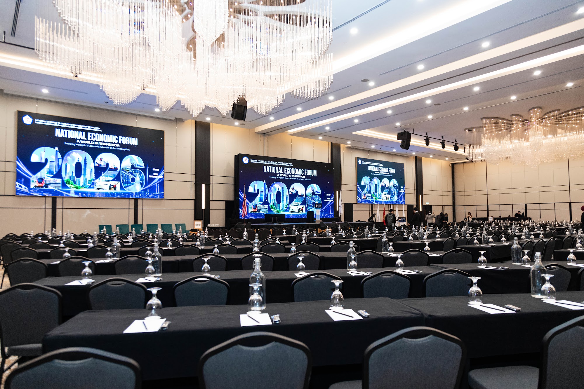 Conference ballroom set up with black linen tables, chairs and LED screens before a business forum