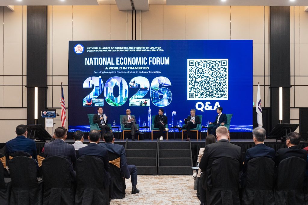 Delegates seated for a conference Q&A session with speakers on stage and a QR code on the LED screen